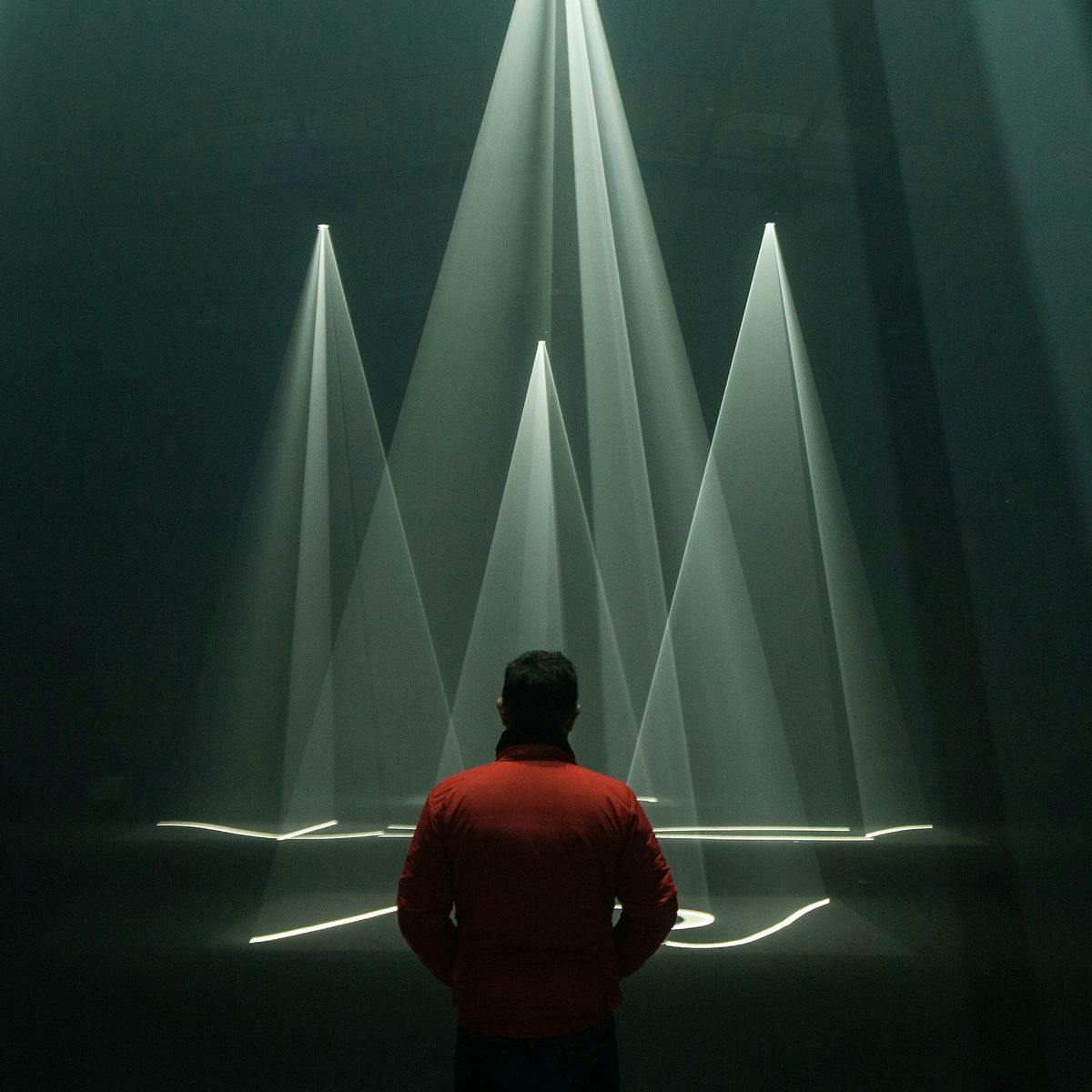 A person wearing a red jacket standing in front of several green triangular light beams.