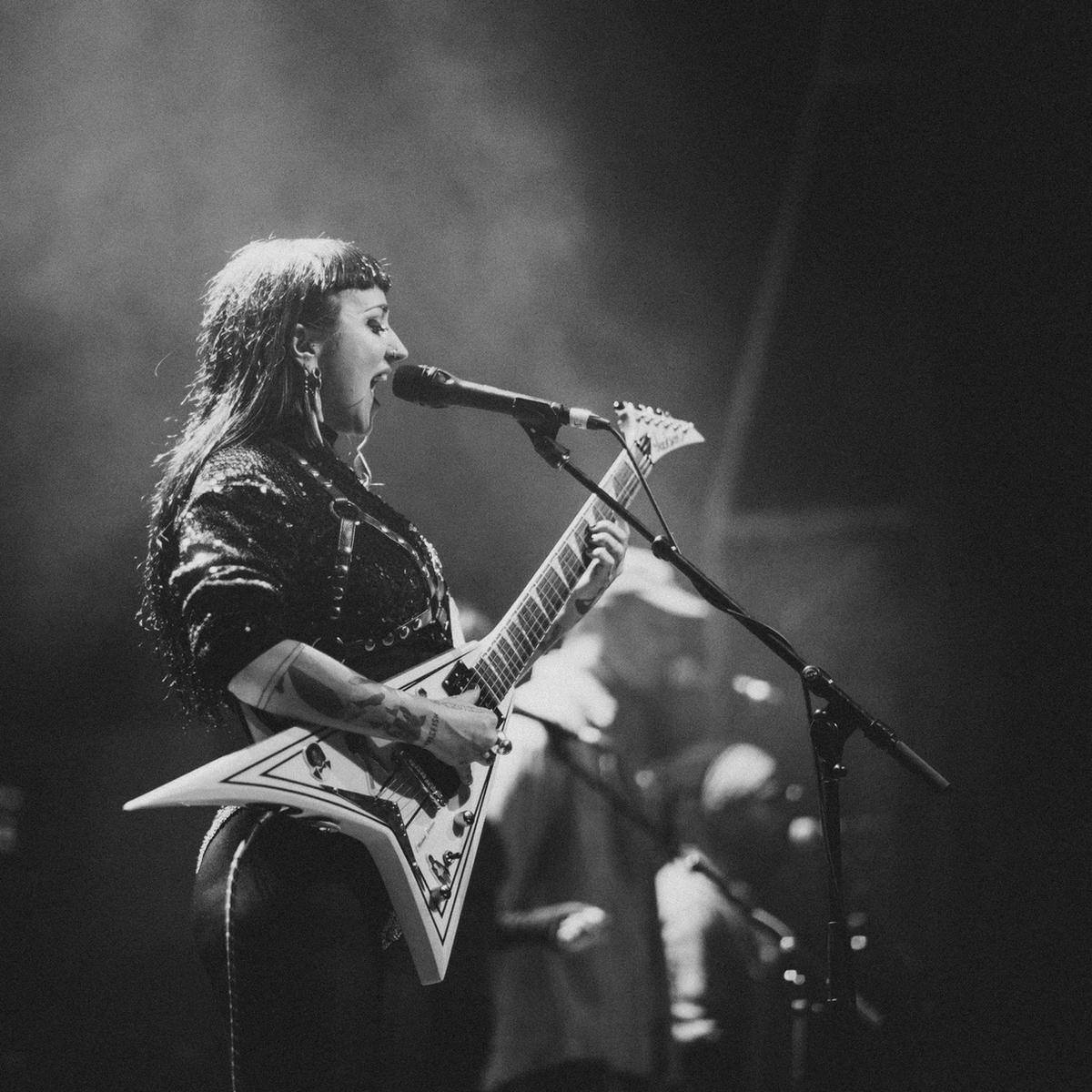 A black and white shot of a person singing and playing guitar on stage.