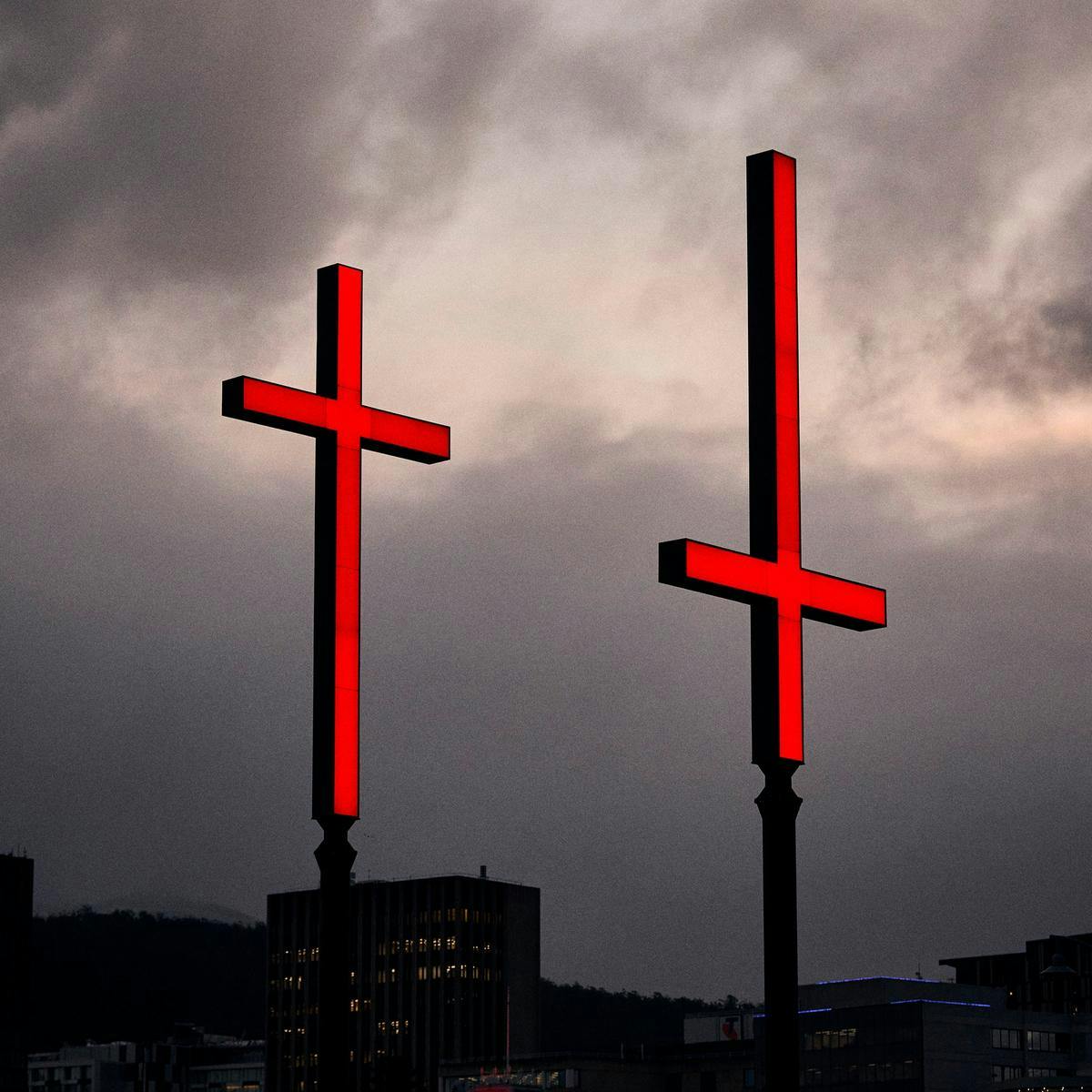 Two large red crosses foreground a clouded Hobart sky. One cross is inverted.