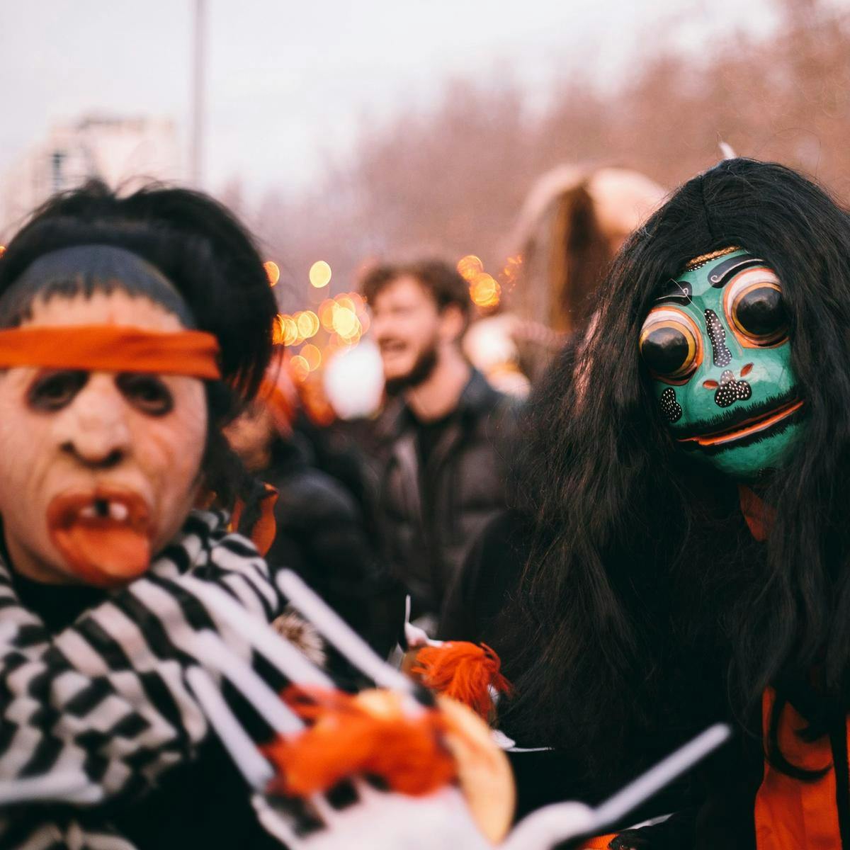 Two people wearing masks, one a disfigured human face, the other a painted frog face with huge eyes.