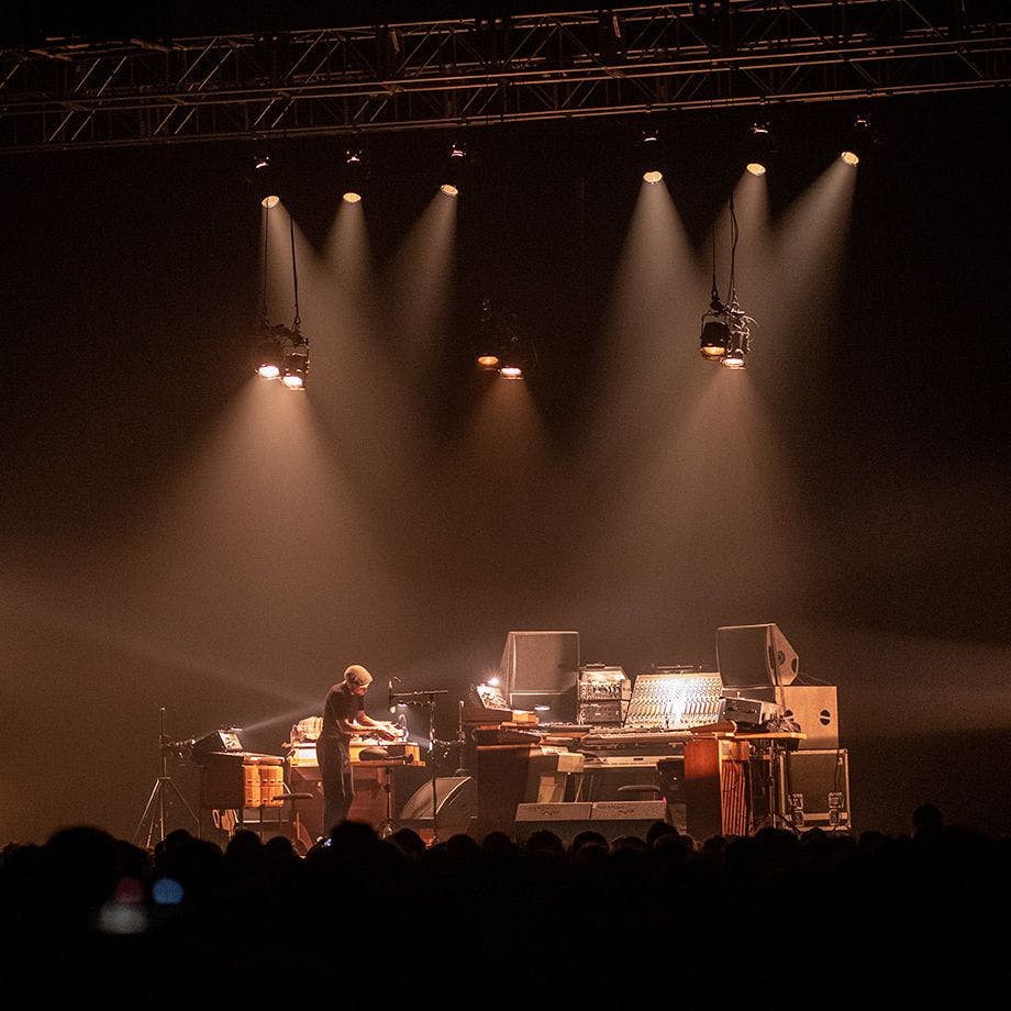 Nils Frahm performing on stage. His extensive setup includes several synths, speakers and mixing boards.