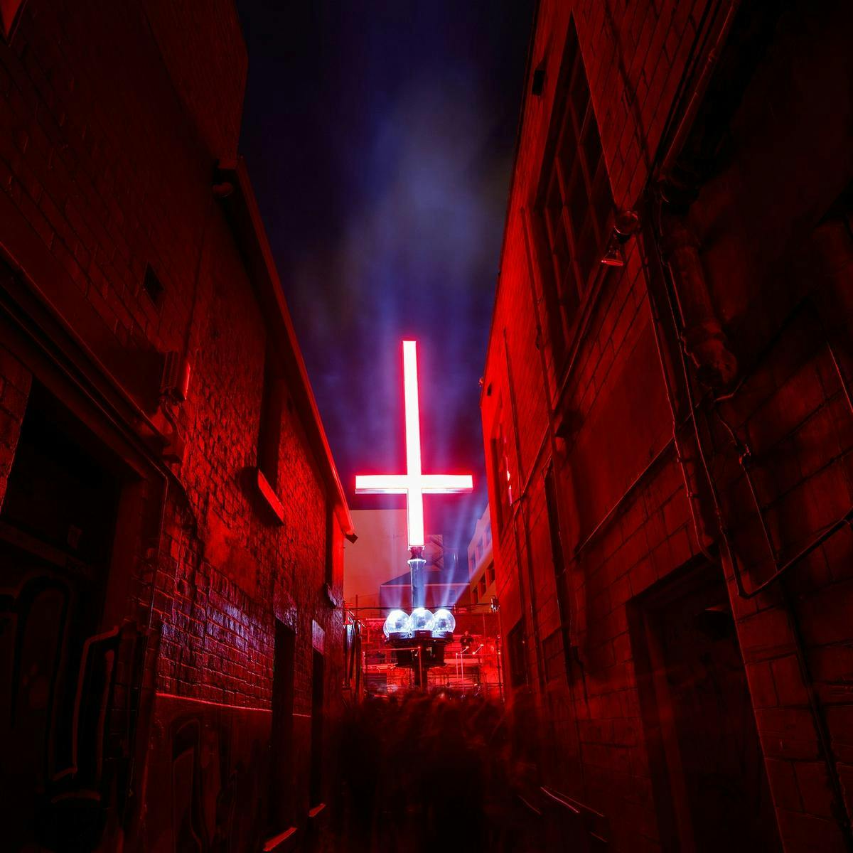 A large inverted red cross lights up a city laneway.