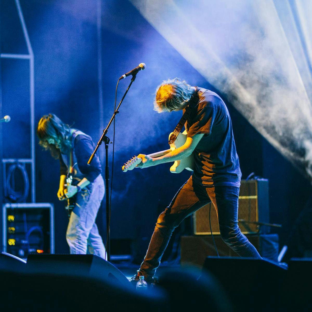 Two people performing guitars on stage.