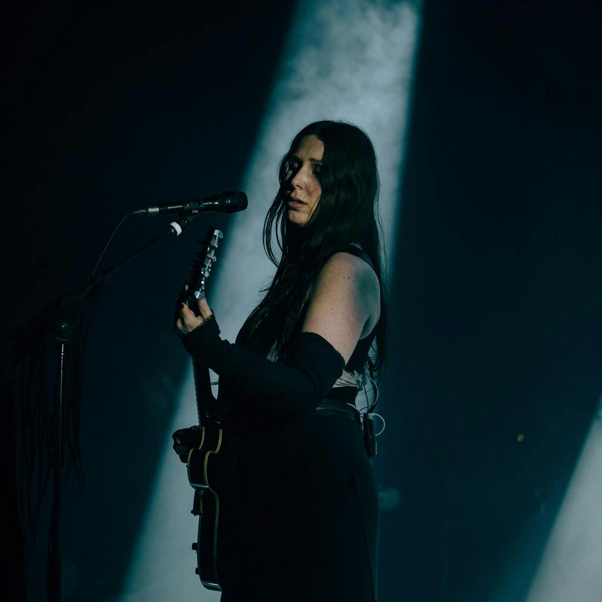 Chelsea Wolfe performs on stage, a singular spotlight lights up the background.