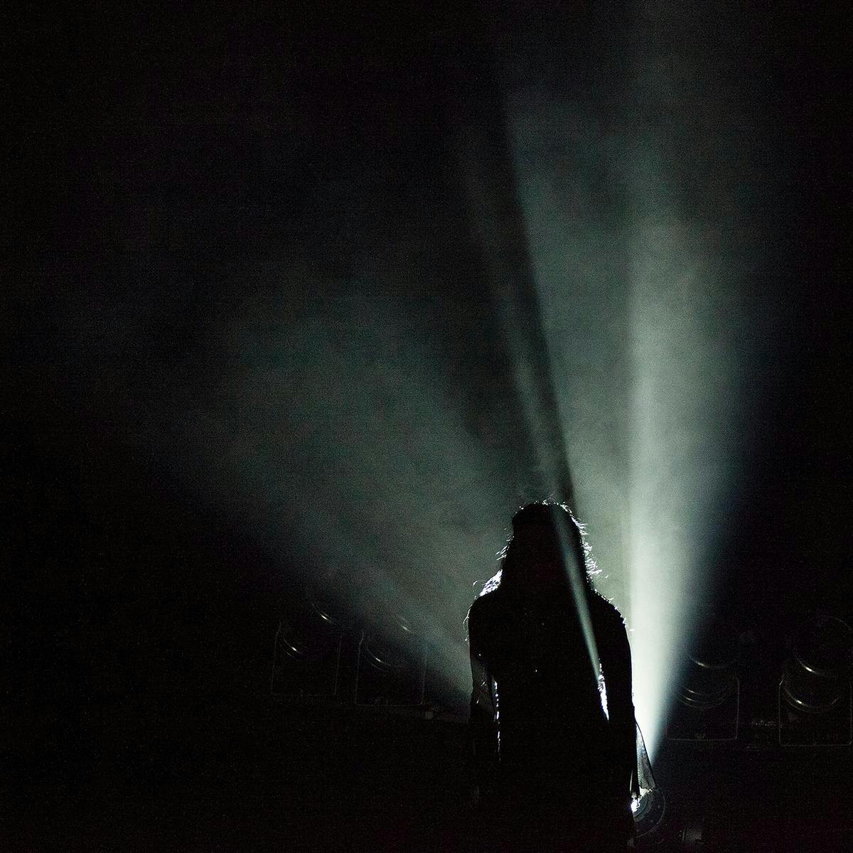 A silhouetted figure is backlit by a bright white spotlight.