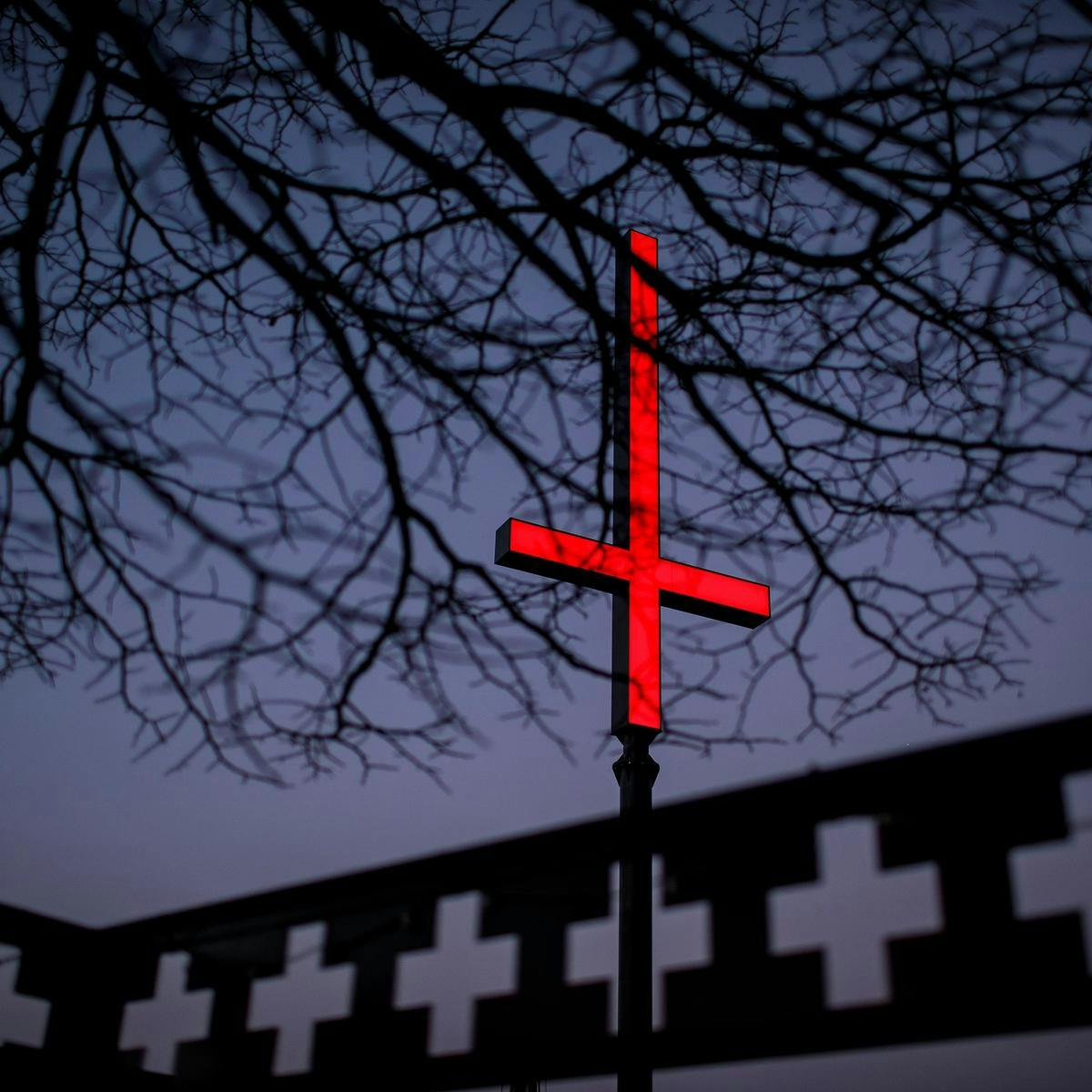 A barren leafless tree obscures a large red inverted cross.