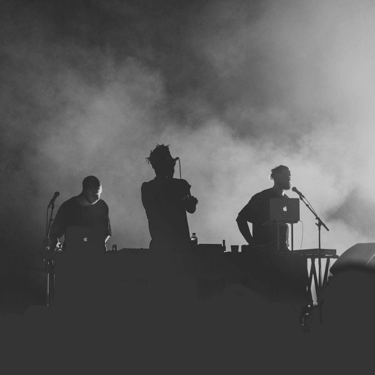 Three silhouetted people on stage performing for a crowd.