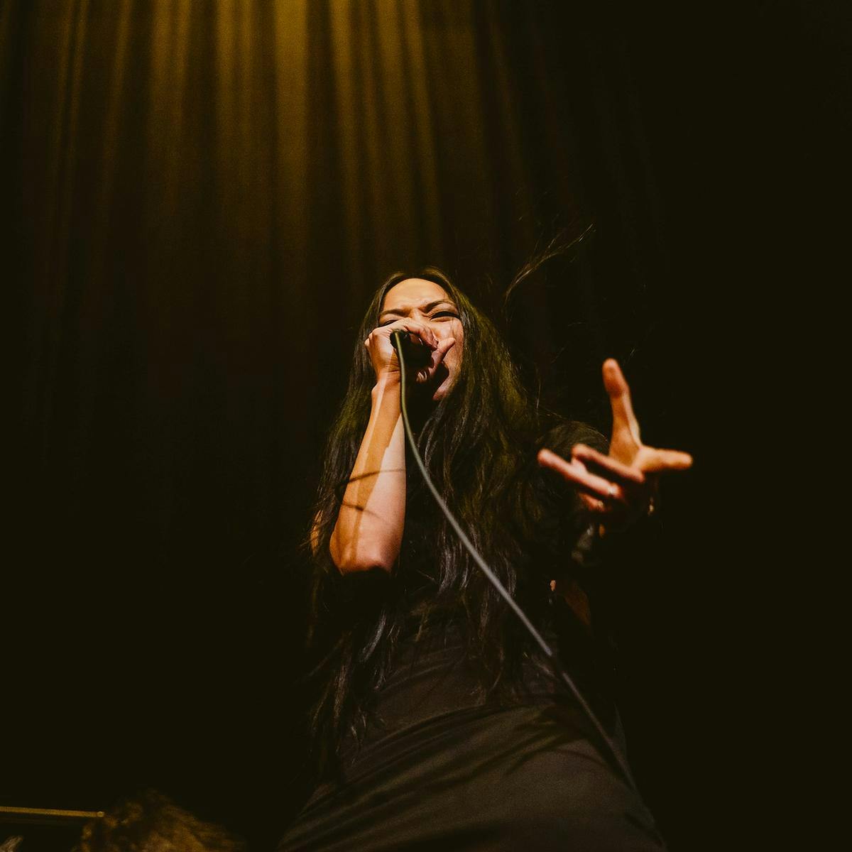 A member of Raja Kirik performs onstage, their hand outstretched towards the camera.