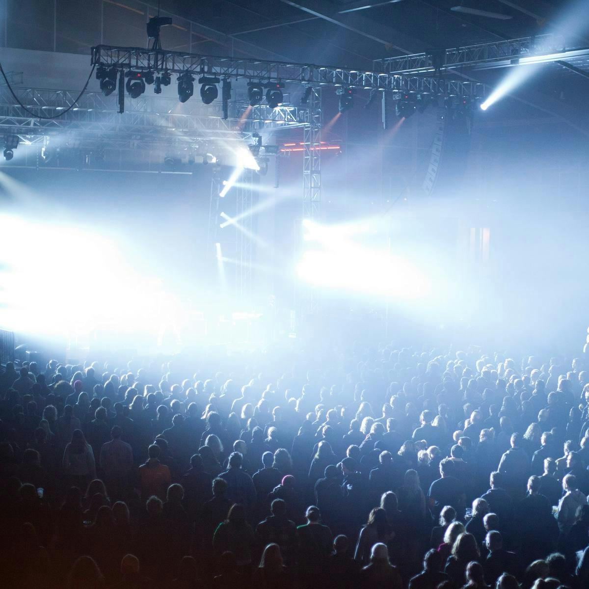 A large crowd standing in front of a stage with bright white lights.