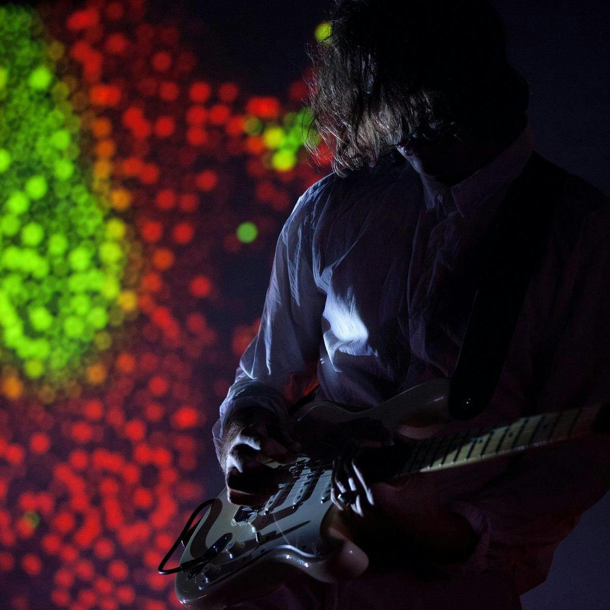 A person playing guitar with green and red lights behind them.