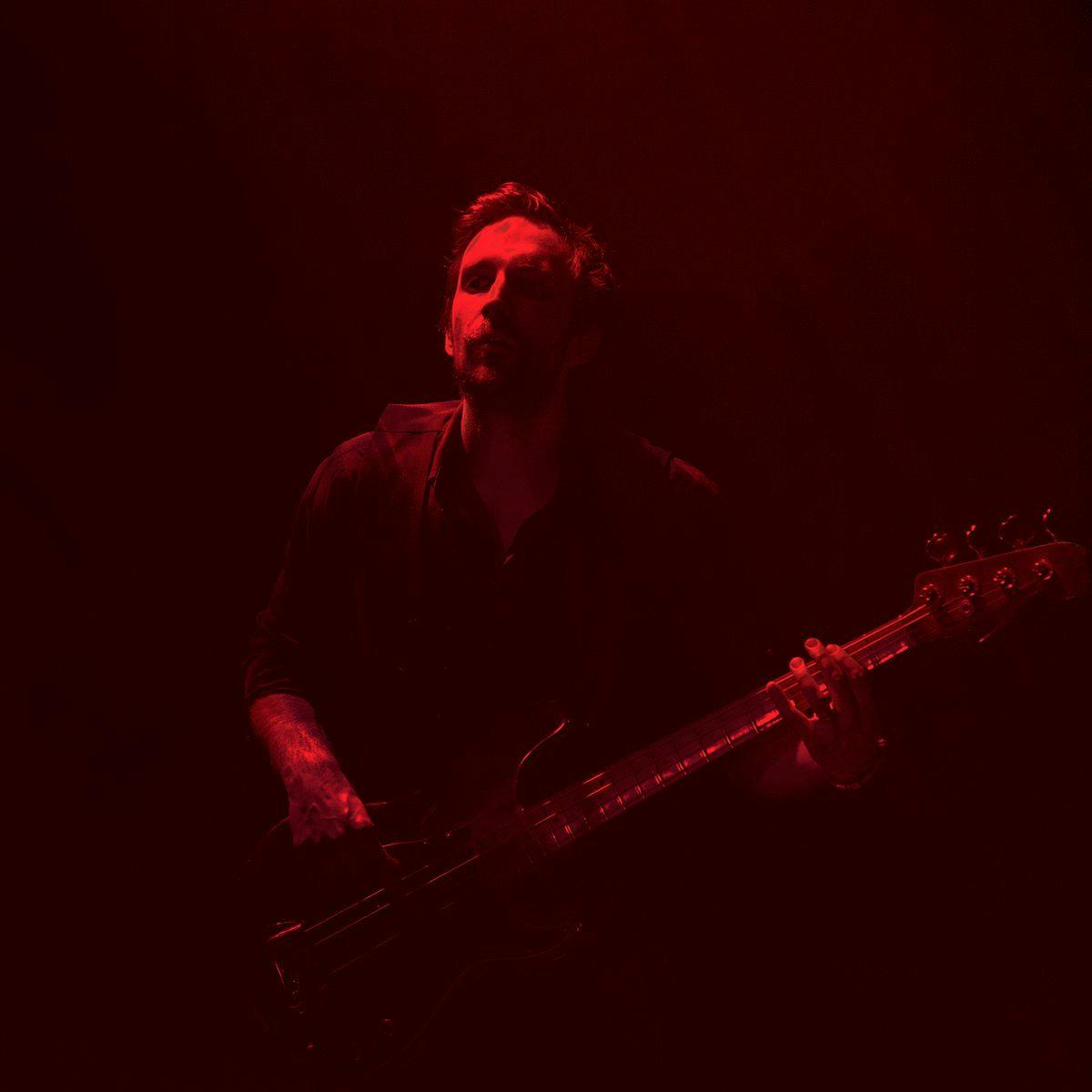 Jeff Lang performs with a guitar, lit up exclusively with red lights.