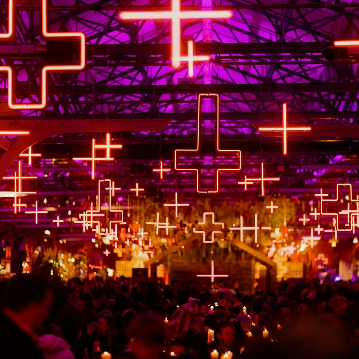 Neon crosses hanging above tables full of people with candles