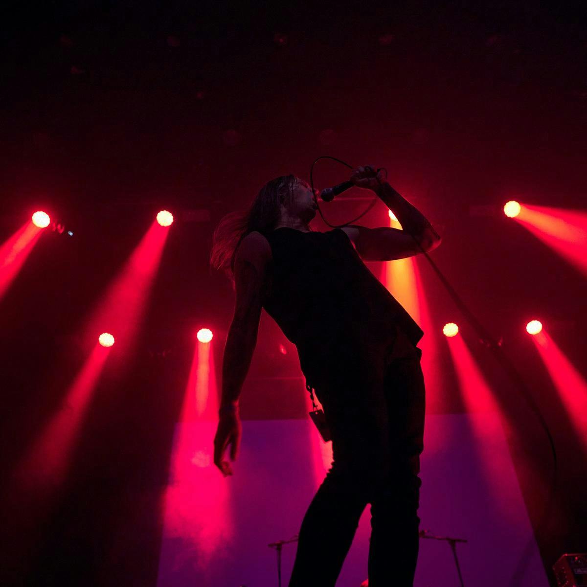 A person performs into a microphone, several red lights beam down onto the stage.