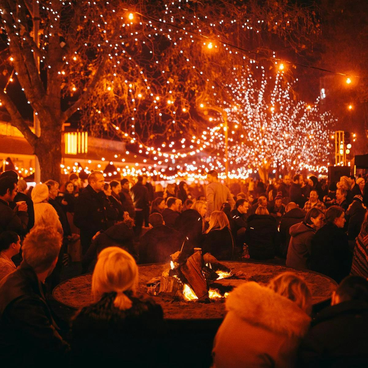 Hundreds of people gather, standing and seated at the Winter Feast. Red fairy lights dominate the background.