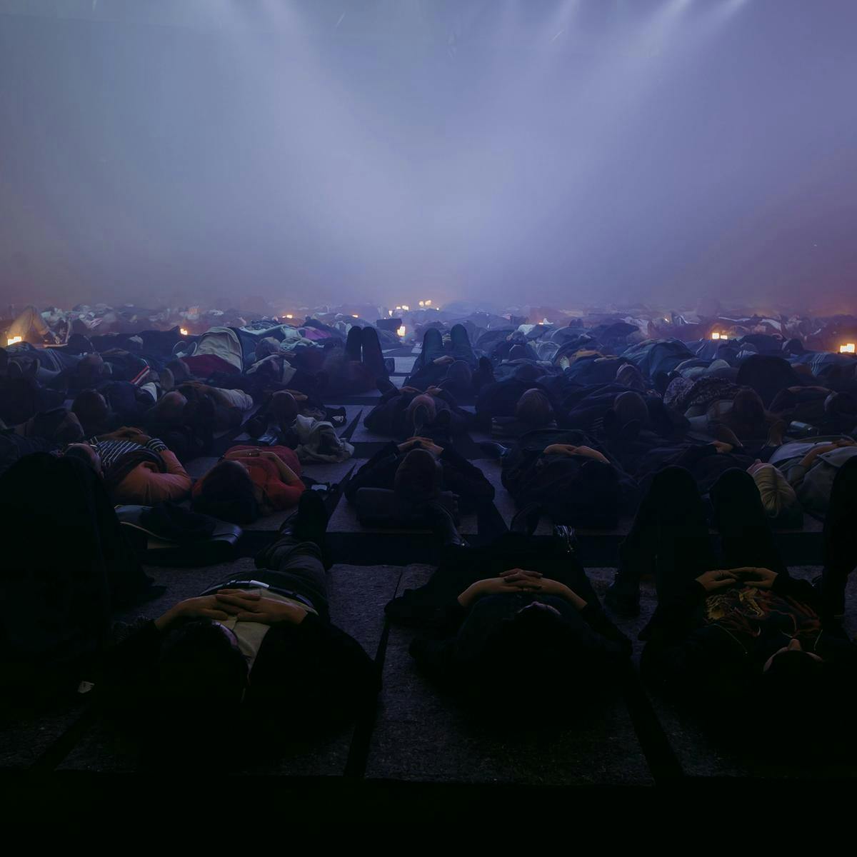 Hundreds of people lay flat on the floor, several candles are scattered amongst the crowd.