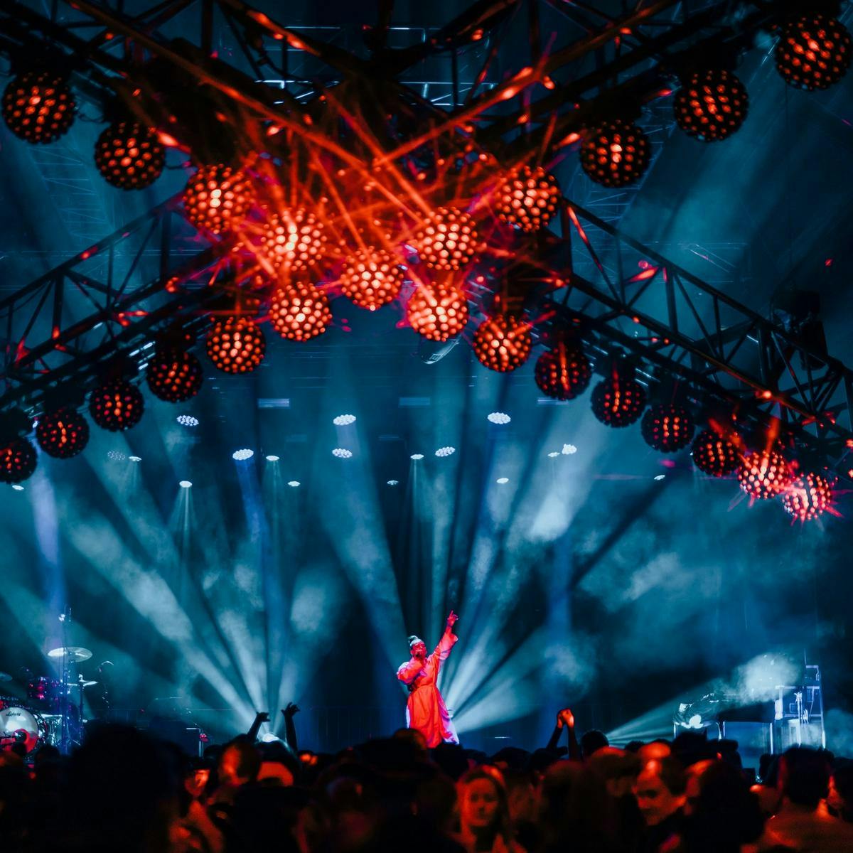 A red cross with round lights hanging above a crowd watching a person on stage