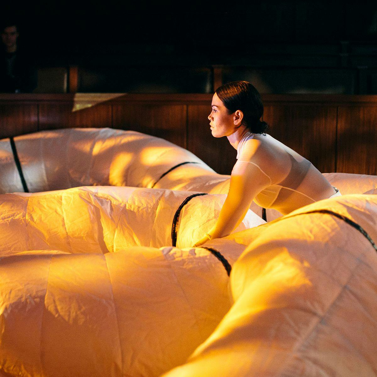 A person crouches down, surrounded by a snake of large white duct-like tubing.