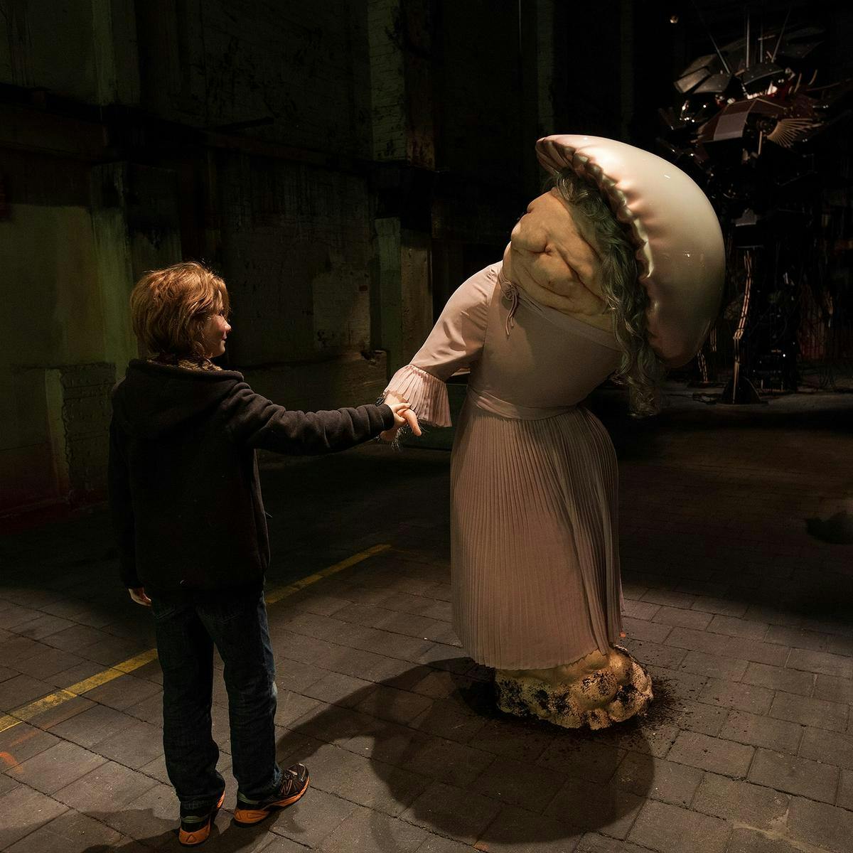 A child reaches out to touch a strange disfigured human-like sculpture.