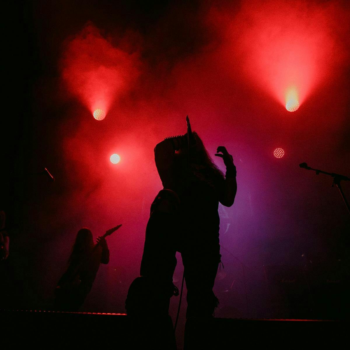 A silhouetted person performs with a microphone, red and purple lights the background.