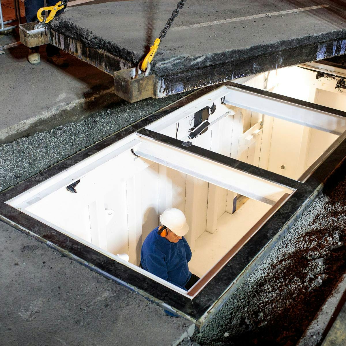 Mike Parr sits in a room inset beneath a road. The lid, to cover the room is being moved into place.