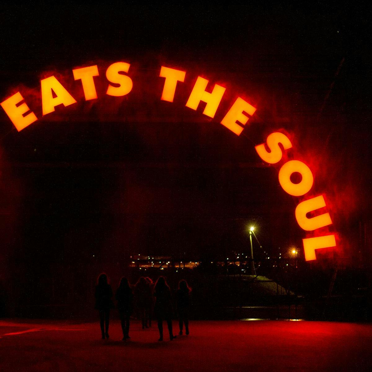 A small group of people walk beneath a large arched sign. The red neon letter read 'Feat Eats The Soul'.