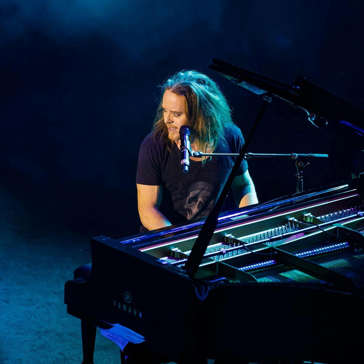 Tim Minchin plays a grand piano.